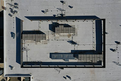 Aerial view of a flat rooftop with rectangular structures, air conditioning units, and various equipment casting shadows, arranged within a dark rectangular border.