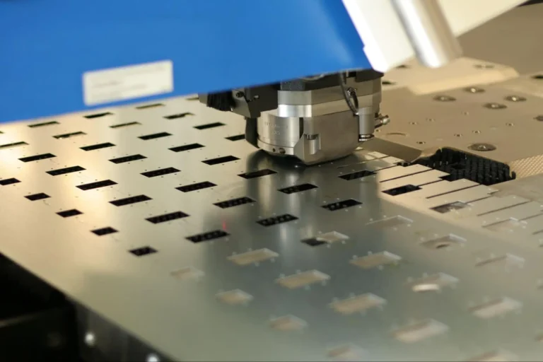 A close-up of an industrial CNC machine cutting rectangular slots into a sheet of metal, with precise, automated movements and a blue protective cover above the cutting tool.