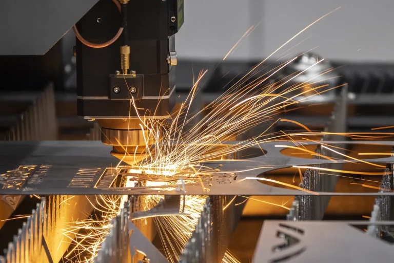 A close-up of a machine cutting metal with a laser, emitting bright orange sparks as it shapes a flat metal sheet in an industrial setting.