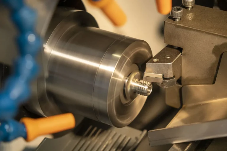 A close-up of a metal lathe machine turning a cylindrical metal piece with a threaded end, highlighting steel fabrication in progress with precision cutting tools and safety guards visible.