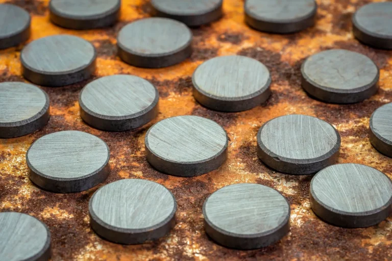 Close-up of several round, metallic discs arranged in a grid pattern on a rusted, textured magnetic sheet metal surface. The smooth, gray discs contrast with the rough, orange-brown background.