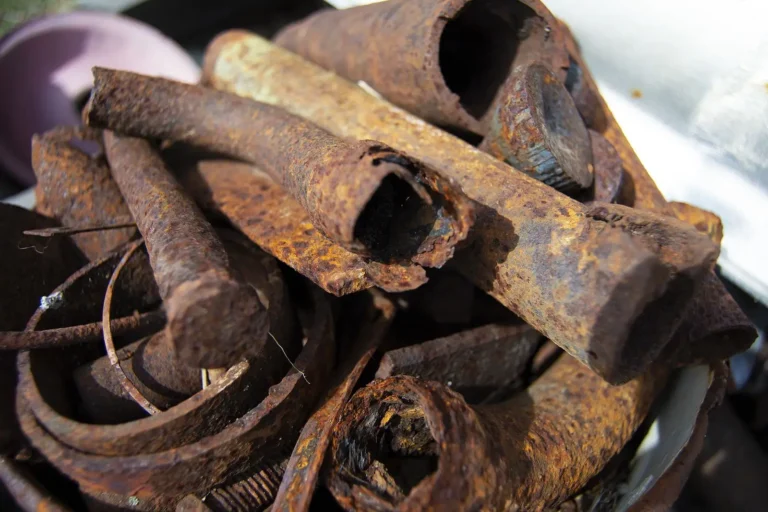A pile of old, rusty metal pipes and scraps in various shapes and sizes, showing rough, corroded surfaces and reddish-brown rust—unlike what metal does not rust, such as stainless steel or aluminum.