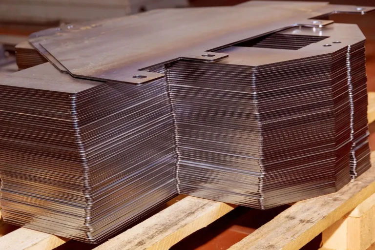 A stack of identical, shiny metal sheets with notched corners sits neatly on a wooden pallet, ready for industrial use or further processing.