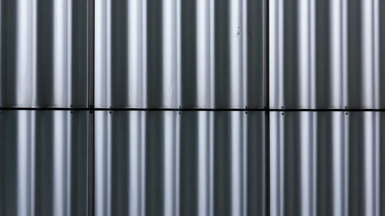 A close-up view of vertical silver metal panels with a corrugated texture, aligned in rows and separated by a horizontal seam and screws visible along the seams.