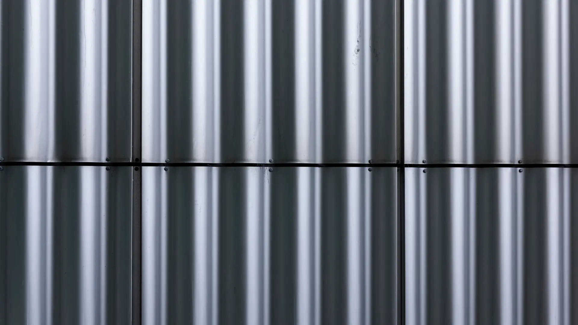 A close-up view of vertical silver metal panels with a corrugated texture, aligned in rows and separated by a horizontal seam and screws visible along the seams.