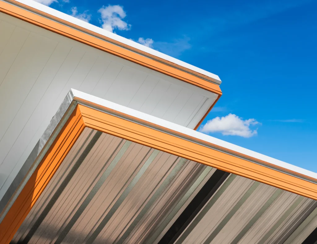 custom metal flashing & trim Close-up view of two modern building roofs with orange trim and metallic surfaces, set against a bright blue sky with a few small white clouds.